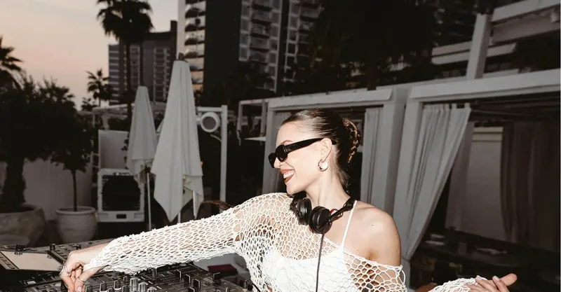 Female DJ in sunglasses and a white crochet top playing a poolside party set in Dubai at sunset